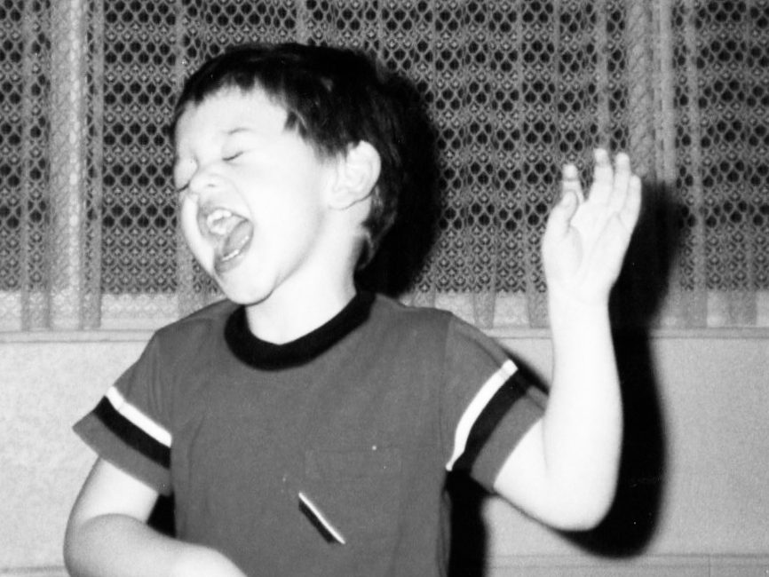 A kid standing with one arm raised and singing.