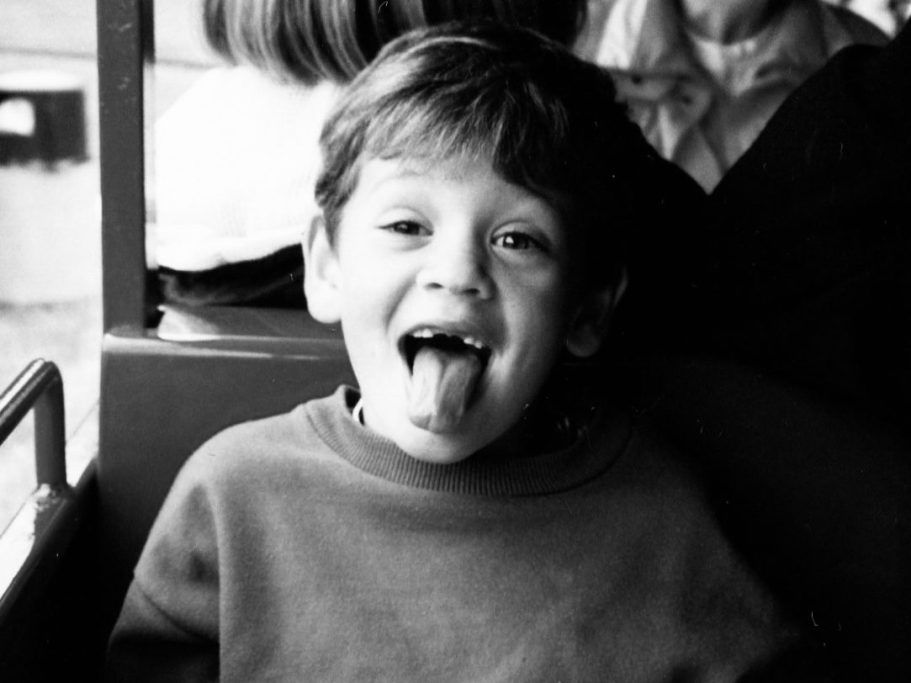 A black and white photo of a child sitting on a train or tram. The child's face is obscured. 